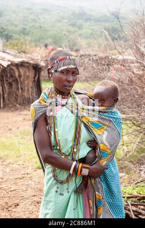 Maasai giovane madre e bambino, con abbigliamento tradizionale, in un villaggio maasai. Riserva Nazionale di Maasai Mara. Kenya. Africa. Foto Stock