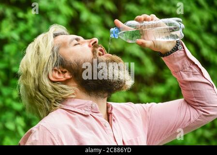Equilibrio dell'acqua. Uomo sopportato turista acqua potabile bottiglia di plastica natura sfondo. Calore estivo. Acqua potabile. Ragazzo assetato che beve acqua in bottiglia. Stile di vita sano. Sicurezza e salute. Foto Stock
