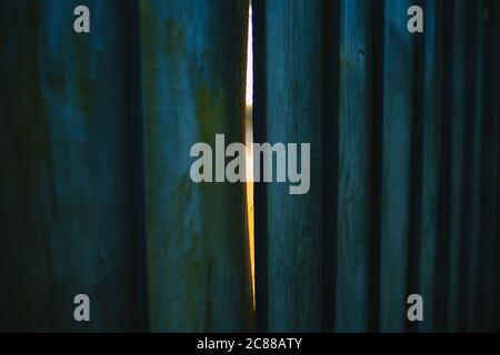Una recinzione in legno dipinta blu con una luce di semina a fessura venendo attraverso - scorci di luce - scorci di speranza Foto Stock