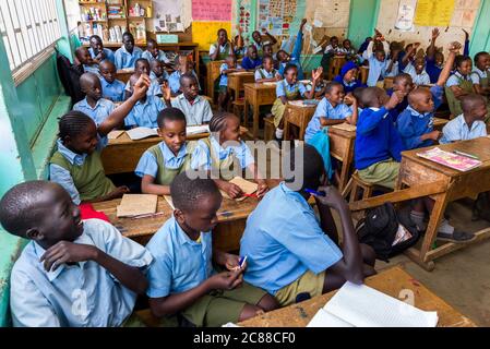I bambini della scuola secondaria in uniforme si sedevano a banchi di legno ascoltando il loro insegnante durante la lezione, Nairobi, Kenya Foto Stock