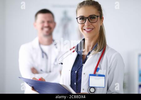 Femmina medico sorridente e tenere appunti da dietro il suo collega è in piedi. Foto Stock