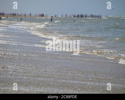 Calme onde sulla spiaggia del mare del nord a Katwijk/NL. Persone lontane in background sfocato Foto Stock