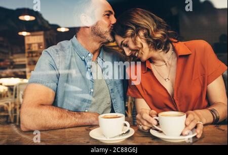 Uomo baciando fronte della sua donna seduto al bar. Coppia innamorata in un appuntamento con il caffè. Foto Stock