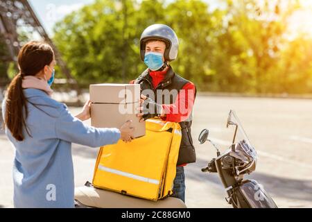 Consegna Guy che dà scatole di cibo a ragazza cliente che si trova all'aperto Foto Stock