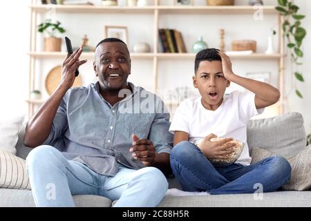Nonno africano e nonno che guardano gli sport in TV, reagendo emotivamente al punteggio Foto Stock