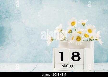 Calendario cubo bianco per agosto decorato con fiori margherita su blu con spazio copia Foto Stock