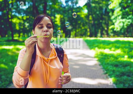 Giovane donna che soffia bolle sulla natura. Una giovane donna bruna felice passeggiava nel parco e fa bolle di sapone in una giornata di sole Foto Stock