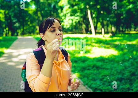 Giovane donna che soffia bolle sulla natura. Una giovane donna bruna felice passeggiava nel parco e fa bolle di sapone in una giornata di sole Foto Stock