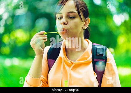 Giovane donna che soffia bolle sulla natura. Una giovane donna bruna felice passeggiava nel parco e fa bolle di sapone in una giornata di sole Foto Stock