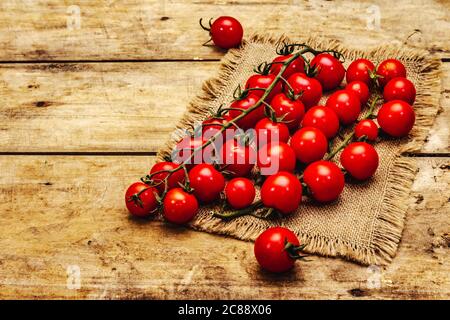 Pomodori ciliegini maturi interi su ramo. Nuova raccolta, su sackcloth, legno sfondo tavole, spazio copia Foto Stock