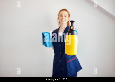 La cameriera dell'hotel, vestita con un panno blu e detergente professionale, si prepara a pulire la camera, avendo un buon umore isolato su uno sfondo bianco Foto Stock