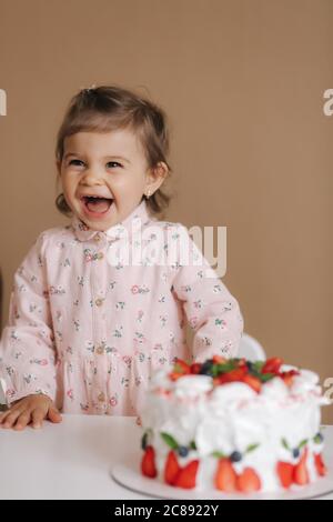 Carino bambina uno e un hulf vecchio stand da deliziosa torta di compleanno. Diciotto mesi ragazza verry felice e ride. Cibo vegetariano. Lattosio Foto Stock