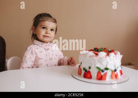 Carino bambina uno e un hulf vecchio stand da deliziosa torta di compleanno. Diciotto mesi ragazza verry felice e ride. Cibo vegetariano. Lattosio Foto Stock