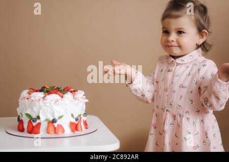 Carino bambina uno e un hulf vecchio stand da deliziosa torta di compleanno. Diciotto mesi ragazza verry felice e ride. Cibo vegetariano. Lattosio Foto Stock