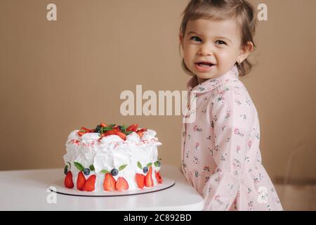 Carino bambina uno e un hulf vecchio stand da deliziosa torta di compleanno. Diciotto mesi ragazza verry felice e ride. Cibo vegetariano. Lattosio Foto Stock