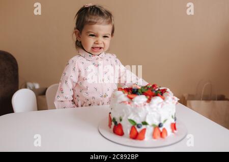 Carino bambina uno e un hulf vecchio stand da deliziosa torta di compleanno. Diciotto mesi ragazza verry felice e ride. Cibo vegetariano. Lattosio Foto Stock