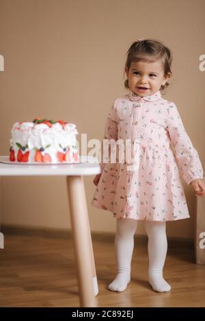 Carino bambina uno e un hulf vecchio stand da deliziosa torta di compleanno. Diciotto mesi ragazza verry felice e ride. Cibo vegetariano. Lattosio Foto Stock