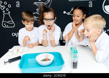 gli studenti adolescenti sono riuniti intorno al tavolo nel laboratorio scolastico e osservano la fase finale del loro esperimento chimico con entusiasmo Foto Stock