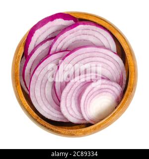 Sezioni trasversali di cipolle rosse in una ciotola di legno. Fette di cipolla Allium cepa con pelle rossa porpora e polpa bianca tinta di rosso. Foto Stock