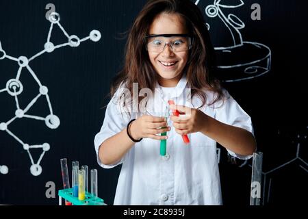 Cute pupilla vietnamita femminile in occhiali protettivi e uniforme bianca, facendo ricerca biochimica in classe chimica Foto Stock