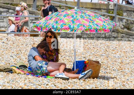 Lyme Regis, Dorset, Regno Unito. 22 luglio 2020. Regno Unito Meteo. I bagnanti e i vacanzieri si affollano sulla spiaggia presso la località balneare di Lyme Regis in Dorset in un altro giorno di sole caldo e bruciante. Un rifugio dal sole caldo sotto un ombrellone. Immagine: Graham Hunt/Alamy Live News Foto Stock