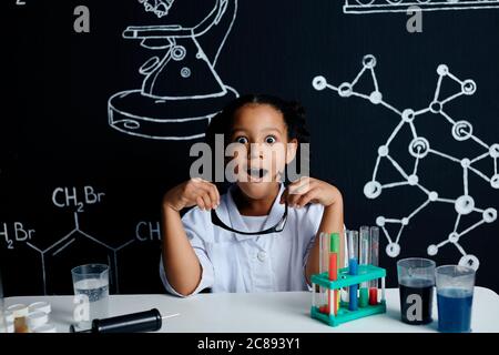 Misto razza asiatica bambina in abiti bianchi scienziato facendo esperimenti scientifici con reagenti in laboratorio, essendo sorpreso e stupito con Foto Stock