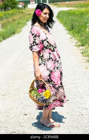 Bella donna brunette in campagna con cesto con fiori Foto Stock