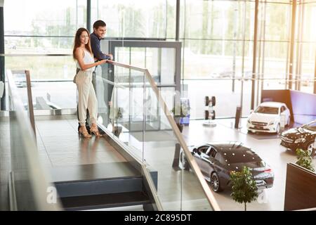 Acquistare la prima auto insieme. Giovane caucasico positivo coppia di riuscito uomo d'affari e sua moglie in piedi in scala alta che guarda sopra il noi Foto Stock