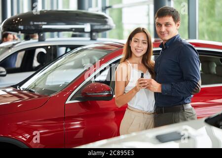 Acquistare la prima auto insieme. Vista ad alto angolo di un venditore di auto professionale in piedi presso la concessionaria con la sua nuova cliente femminile che acquista un lusso ca Foto Stock