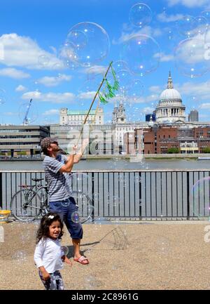 Londra, Inghilterra, Regno Unito. Street intrattenitore sulla South Bank soffia bolle per i bambini a inseguire Foto Stock