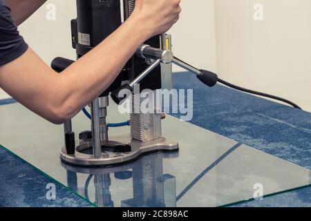 Un lavoratore perfora un foro nel vetro. Foto Stock