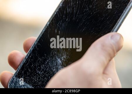 Un giovane ha un telefono con un touch screen molto incrinato Foto Stock