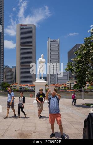 Scellini davanti alla statua di Sir Thomas Raffles sul fiume Singapore con grattacieli e negozi sullo sfondo Foto Stock