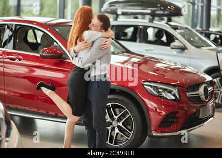 Immagine colorata ed emotiva di felice coppia giovane allegra che celebra l'acquisto di una nuova auto presso la concessionaria Foto Stock