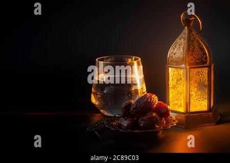 Tradizione religiosa musulmana, mese santo del Ramadan, Islam e tema di concetto di Iftar con una ciotola di date, perle di preghiera, bicchiere d'acqua e lanterna arabica Foto Stock