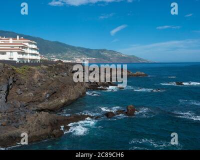 Vista sulla riva del mare con scogliere di roccia lavica al villaggio di Los Cancajos, oceano e verdi colline. Sfondo blu cielo. La Palma, Isole Canarie, Spagna Foto Stock