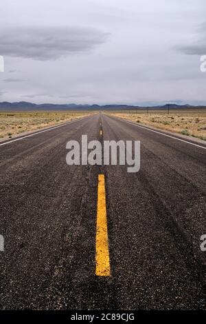 Foto verticale che guarda lungo un tratto solitario dell'autostrada 6 sotto i cieli sovrastati nella contea di Nye, Nevada Foto Stock