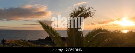 Vista panoramica sulla splendida alba arancione sul tranquillo oceano con la silhouette di foglie di palme a Los Cancajos sull'isola la Palma, Isole Canarie. Foto Stock