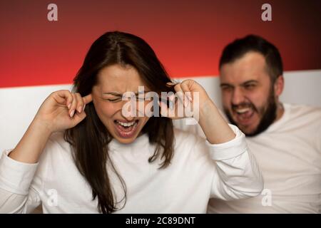 il ragazzo grida sulla ragazza a letto. la ragazza gridando mette le dita in orecchie Foto Stock