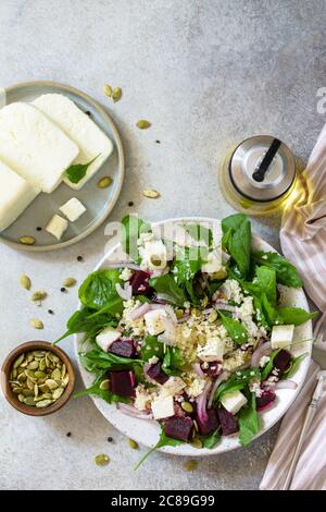 Insalata sana con couscous, formaggio morbido, barbabietola e condimento vinaigrette. Vista dall'alto sfondo piatto. Spazio di copia. Foto Stock