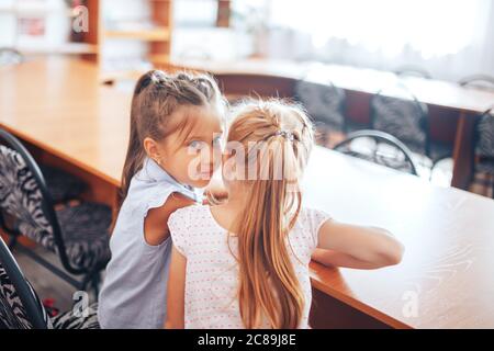 Due studentesse si siedono a un banco della scuola e discutono lo scopo della lezione Foto Stock