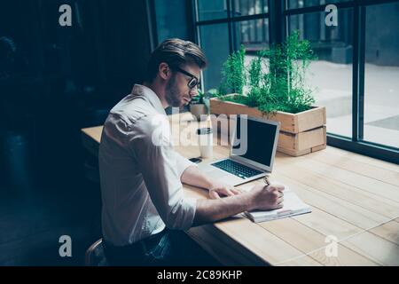 Vista posteriore di un giornalista elegante ragazzo scrivere una storia in un posto di lavoro in loft stile coworking, ben vestito, in occhiali Foto Stock