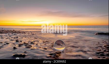 Ghiaia su una spiaggia al tramonto, palla di cristallo, atmosfera zen. Lensball. Foto Stock