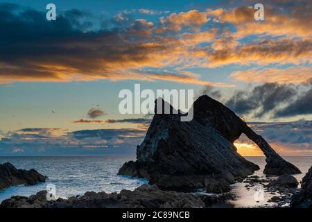 ARCO VIOLINO ROCCIA PORTKNOCKIE MORAY COSTA SCOZIA LUGLIO ALBA NUVOLE COLORATE ORO SOTTO L'ARCO Foto Stock