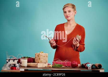 Designer professionista donna che guarda la macchina fotografica mentre insegna agli studenti su confezione regalo, isolato in studio su sfondo blu. Foto Stock