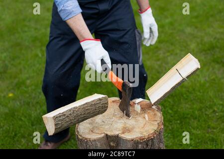 Uomo adulto tagliando legno con ascia in casa privata di campagna. Pezzi volanti di legno Foto Stock