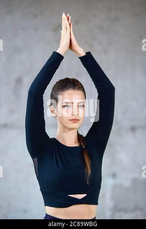 Ritratto di splendida ragazza che pratica yoga in sala fitness, facendo esercizio, praticare la posa albero. Giovane donna in forma che indossa abiti sportivi neri che si allungano in palestra e guardando da parte, interno soppalco. Foto Stock