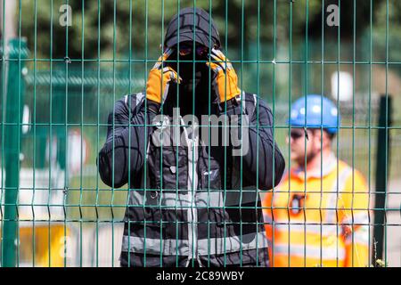 Harefield, Regno Unito. 22 luglio 2020. Una guardia di sicurezza mascherata HS2 osserva un fotografo della stampa durante i lavori per il collegamento ferroviario ad alta velocità HS2 vicino a Harvil Road. Gli attivisti ambientali della HS2 Rebellion e della Stop HS2 continuano a protestare contro la HS2, che attualmente è prevista per costare £106 miliardi e rimarrà un contributo netto alle emissioni di CO2 durante i suoi 120 anni di vita previsti, da una serie di campi di protezione della fauna selvatica lungo il suo percorso. Credit: Mark Kerrison/Alamy Live News Foto Stock