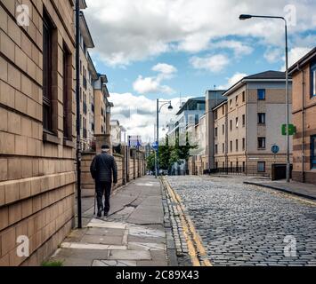 Un anziano con un bastone cammina lungo High Riggs, Fountainbridge, Edimburgo, Scozia, Regno Unito. Foto Stock