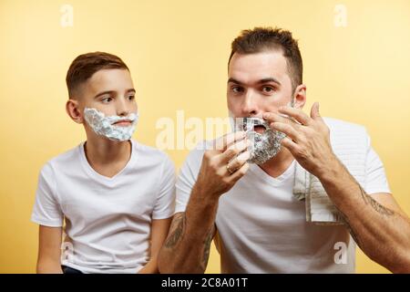 Padre insegnando al figlio come radersi su sfondo giallo Foto Stock